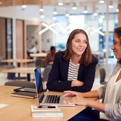 two-businesswomen-with-laptop-at-desk-in-open-plan-office-collaborating-on-project-together